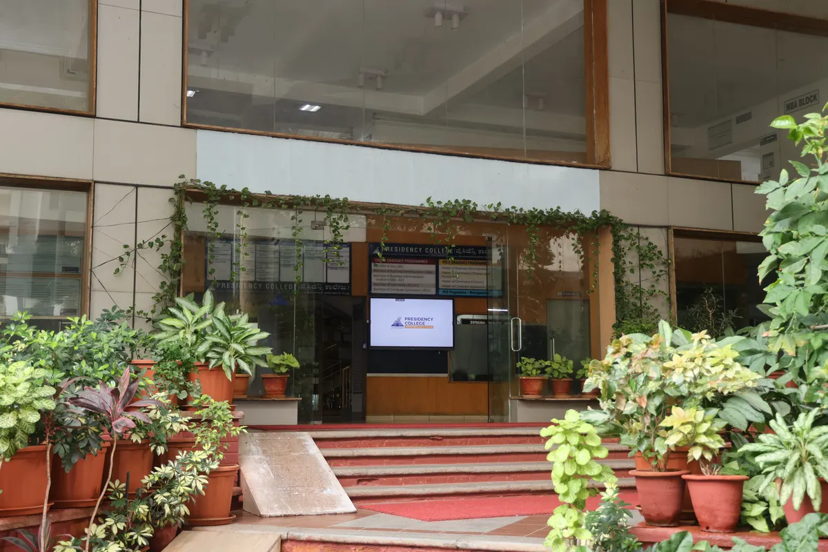The entrance to the college block, with potted plants on the steps and a glass door.