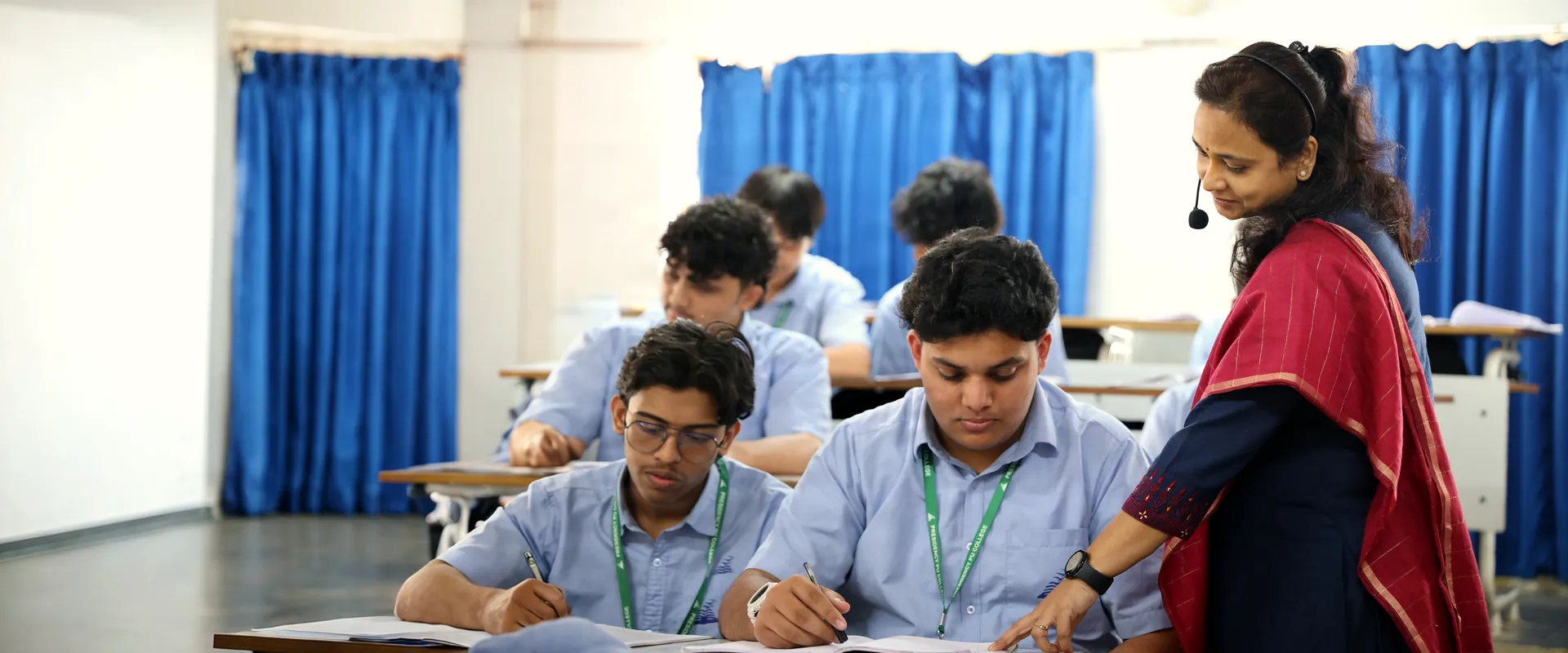 A teacher leans over to check a student's notebook during class.