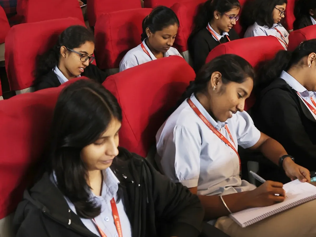 Presidency PU students seated in the auditorium at an Integrated orientation, one taking notes.