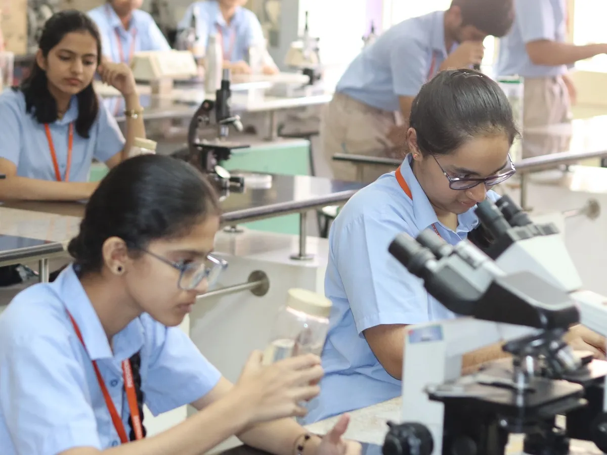 Presidency PU students in the biology lab, one looking into a microscope while another holds a specimen jar.