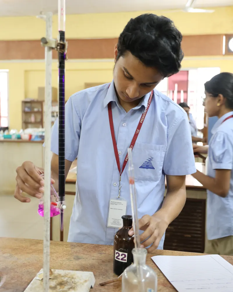 A Presidency PU student in the chemistry lab, looking down as he titrates a pink solution from a burette into a flask.